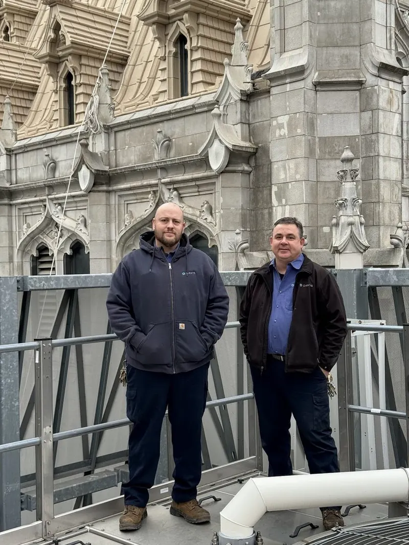 Two building engineers on the roof beside the Gothic spires