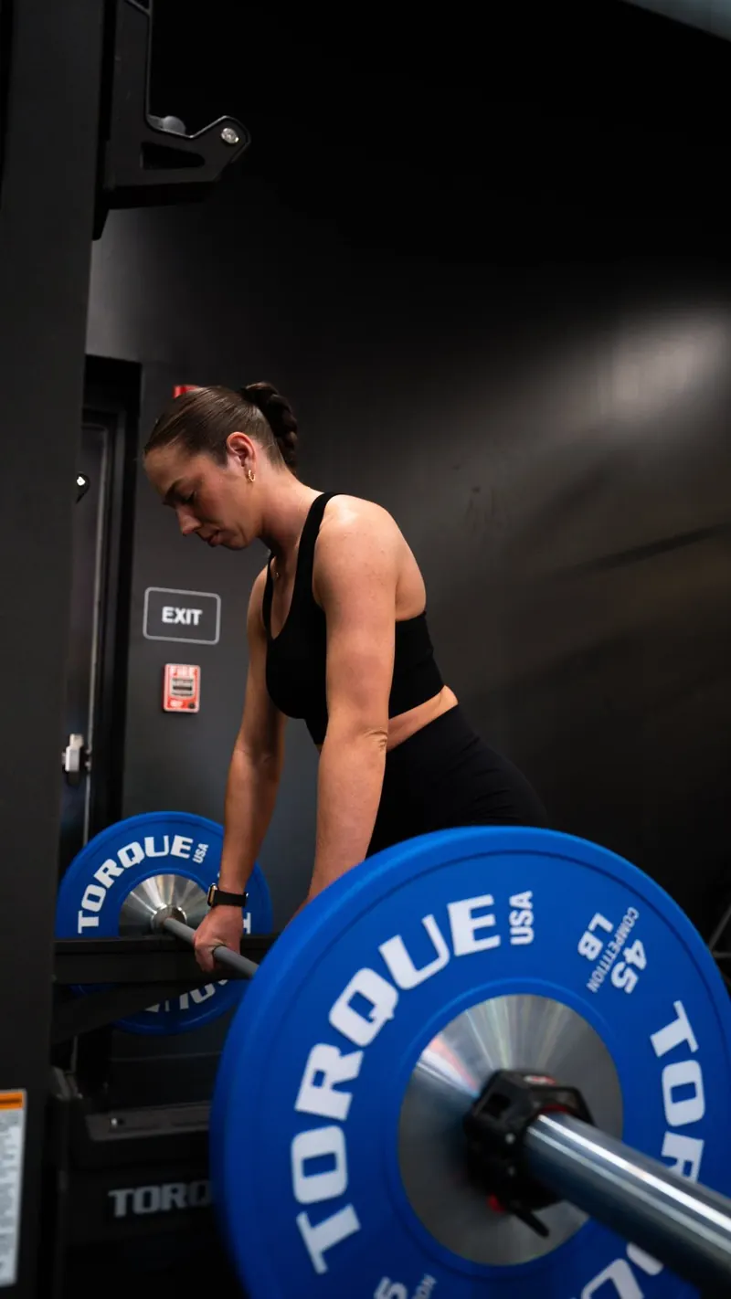 Member gripping a barbell loaded with blue Torque 45 lb plates at the bottom of a deadlift