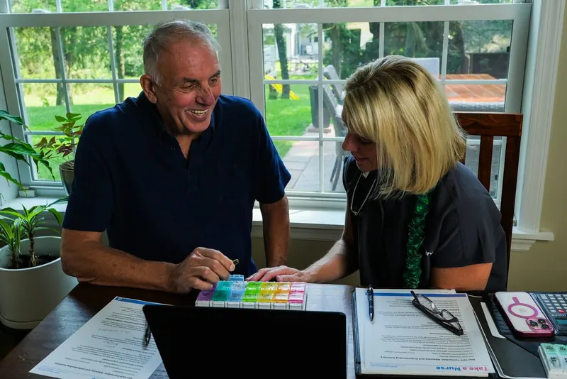 Take a Nurse nurse and client working through a weekly pill organizer at the kitchen table