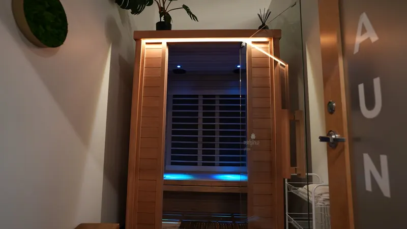 Cedar infrared sauna cabin glowing under warm strip lighting, seen through the open frosted-glass sauna door