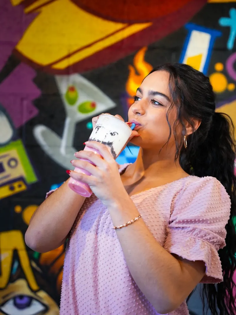 Creator sipping a cookies-and-cream bubble tea through a blue straw in front of Dr. Tea's graffiti mural