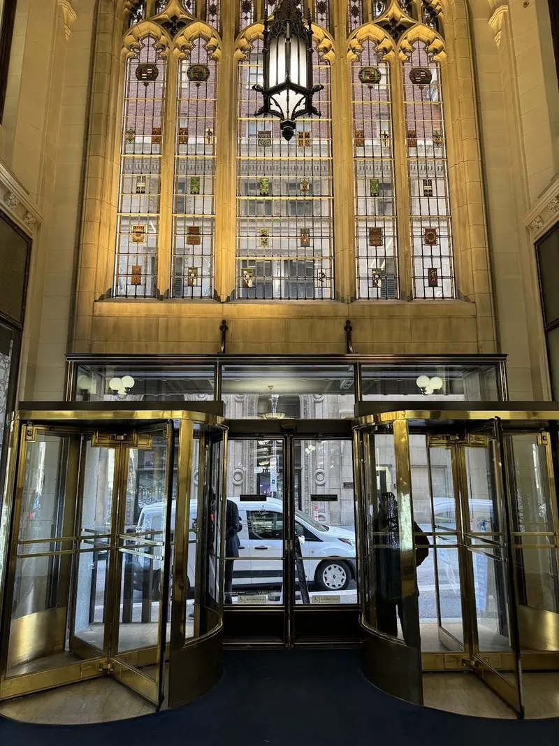 Stained-glass window glowing over the brass revolving doors of the main entrance