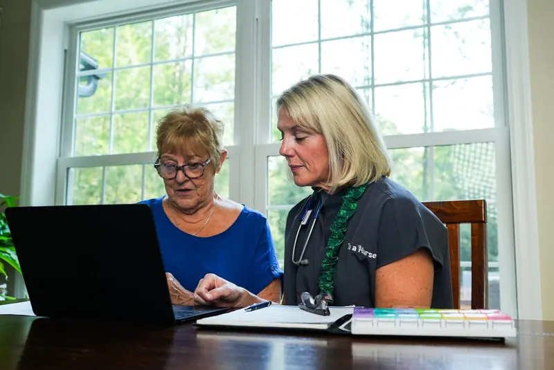 Kathy Fadgen and a client review paperwork at a laptop in window light, a weekly pill organizer on the table