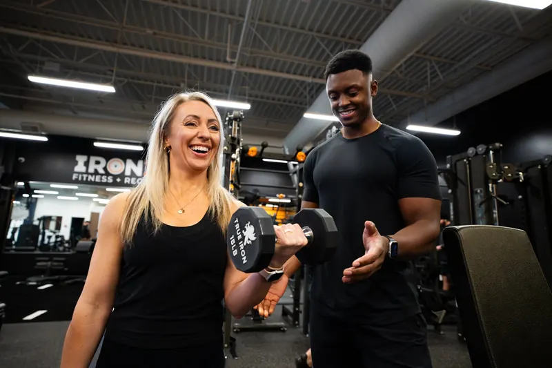 Trainer coaching a member through a dumbbell curl at Iron 24