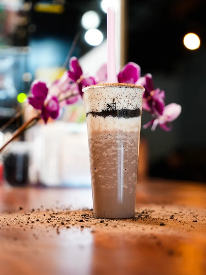 Dr. Tea's layered cookies-and-cream bubble tea with a pink straw on the wooden counter, a magenta orchid behind it