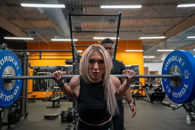Member back-squatting a barbell with blue Torque plates while a trainer spots from behind